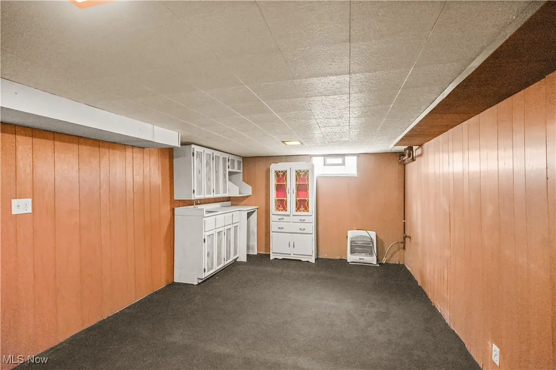 Basement featuring wood walls, dark carpet, and heating unit