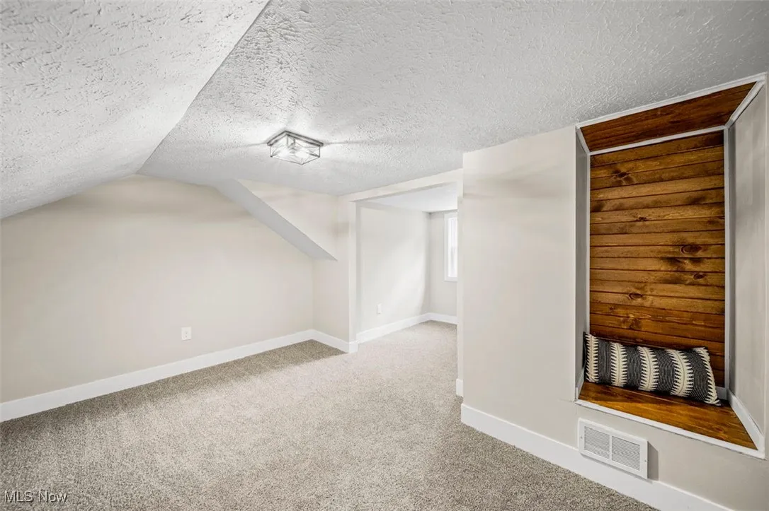 Additional living space with light colored carpet and a textured ceiling
