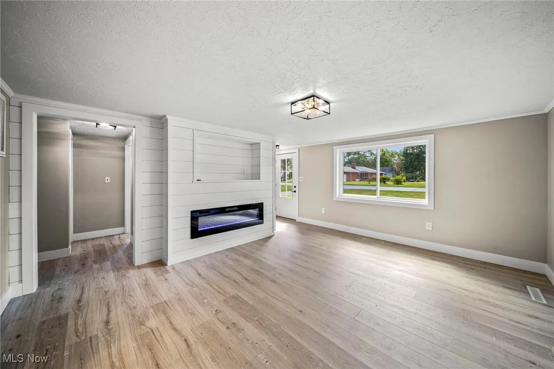 Unfurnished living room with a large fireplace, light wood finished floors, a textured ceiling, and ornamental molding