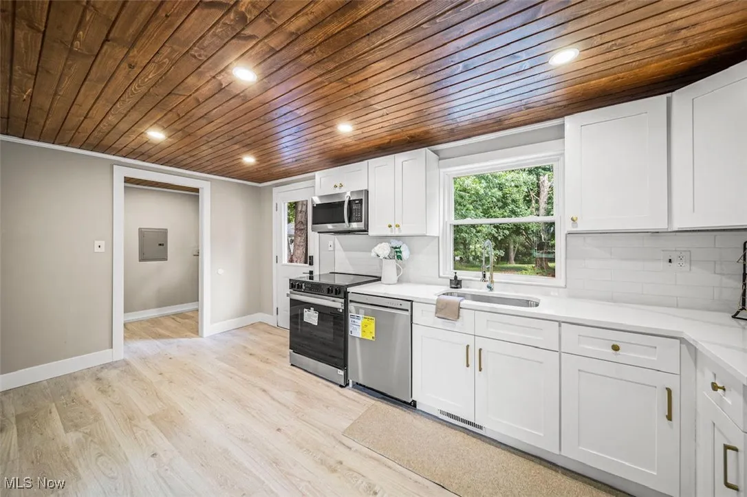 Kitchen featuring wooden ceiling, healthy amount of natural light, white cabinetry, decorative backsplash, and stainless steel appliances