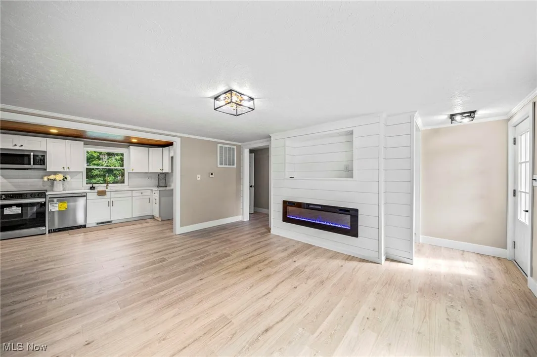 Unfurnished living room with ornamental molding, a fireplace, light wood-style flooring, and a textured ceiling
