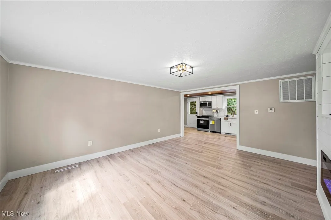 Unfurnished living room with light wood-type flooring and crown molding