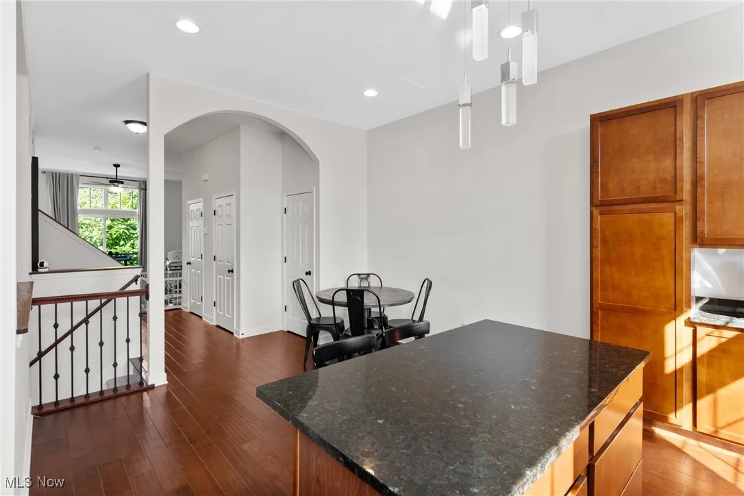 Kitchen with dark wood-style flooring, a kitchen island, arched walkways, dark stone countertops, and recessed lighting