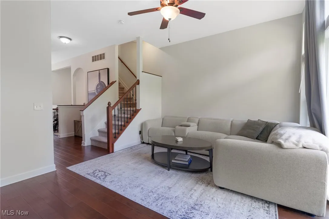 Living area with stairway, dark wood-style floors, arched walkways, and ceiling fan