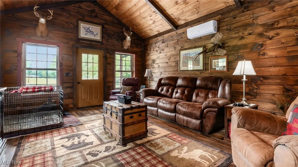 Living room featuring a wooden ceiling with exposed beams, hardwood / wood-style flooring, wooden walls, a wall unit AC, and high vaulted ceiling