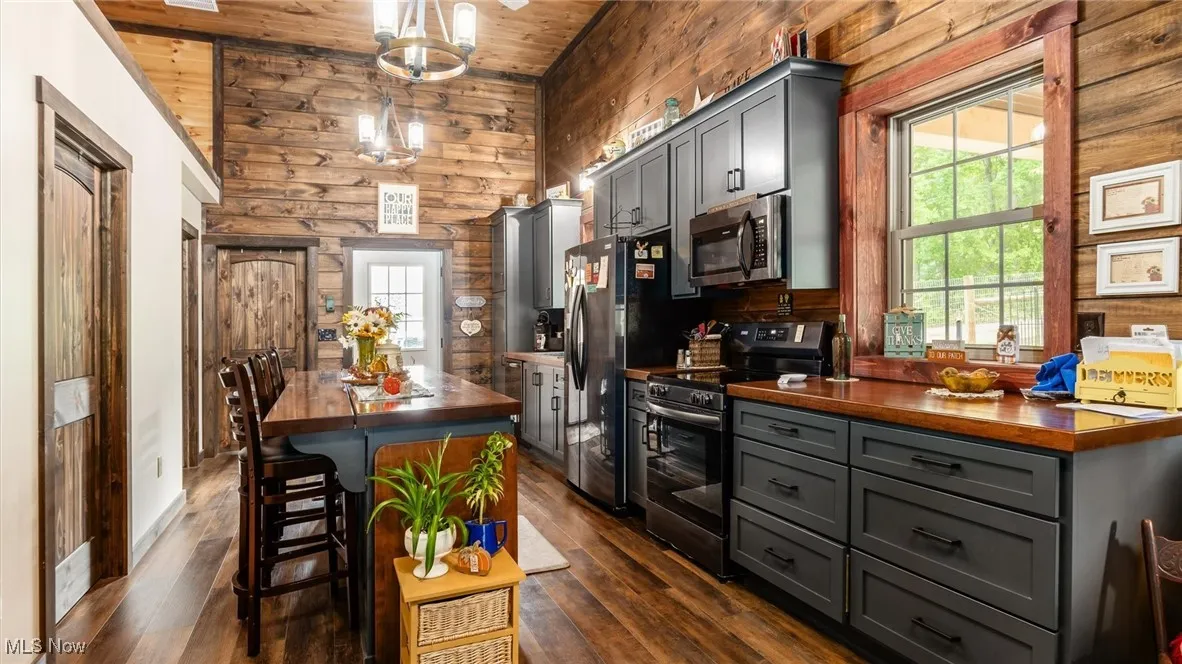 Kitchen featuring gray cabinetry, wooden counters, stainless steel appliances, a center island, and wooden walls