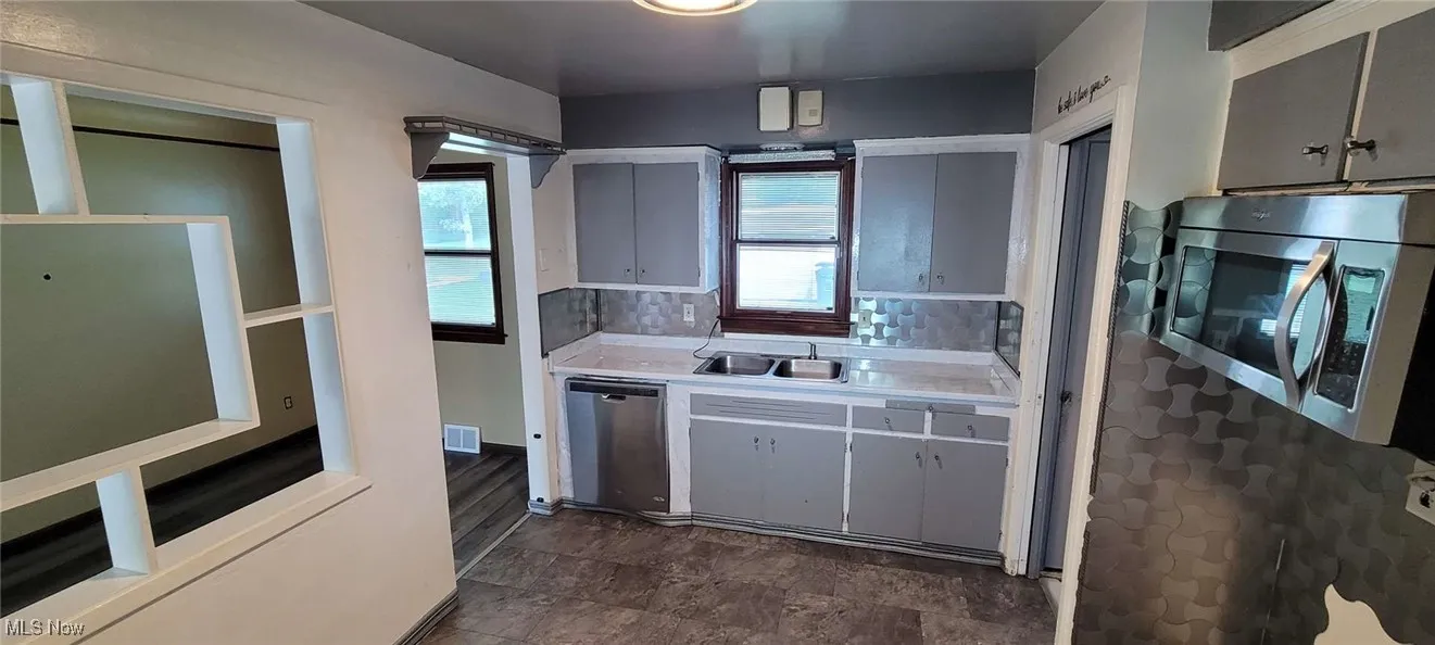 Kitchen with light countertops, stainless steel appliances, decorative backsplash, white cabinets, and gray cabinetry
