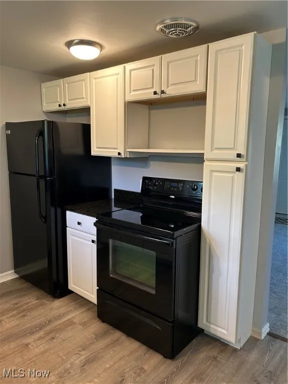 Kitchen featuring black range, white cabinetry, light wood-type flooring, fridge, and dark stone counters
