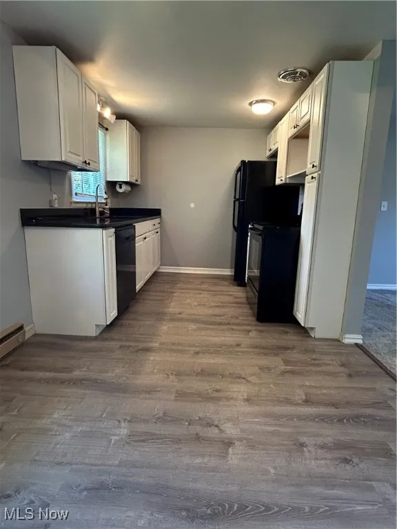 Kitchen with dark countertops, white cabinets, dark wood-type flooring, and dishwasher