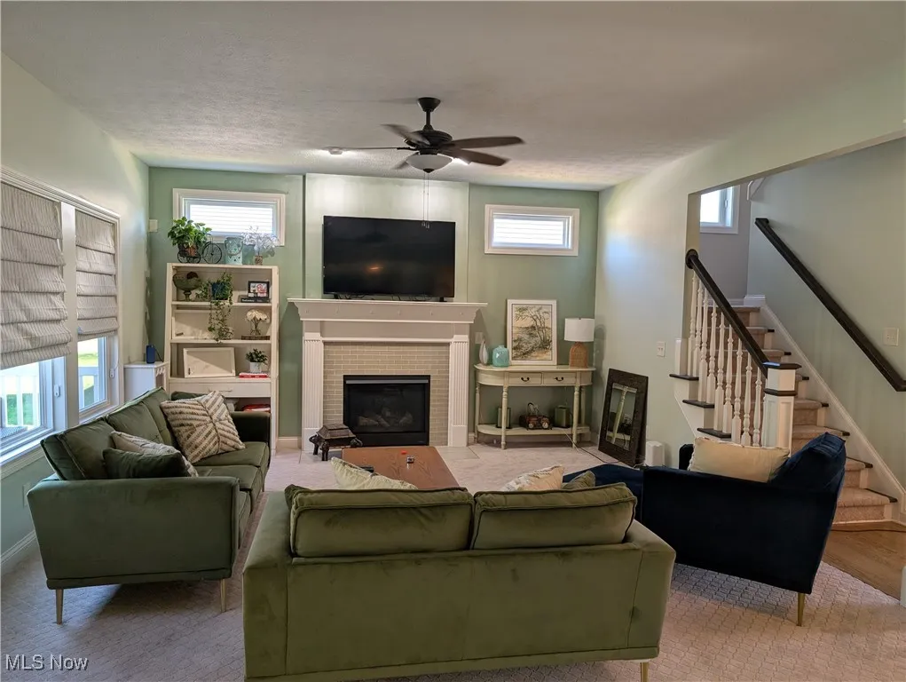 Living area with stairs, a brick fireplace, a ceiling fan, and a textured ceiling