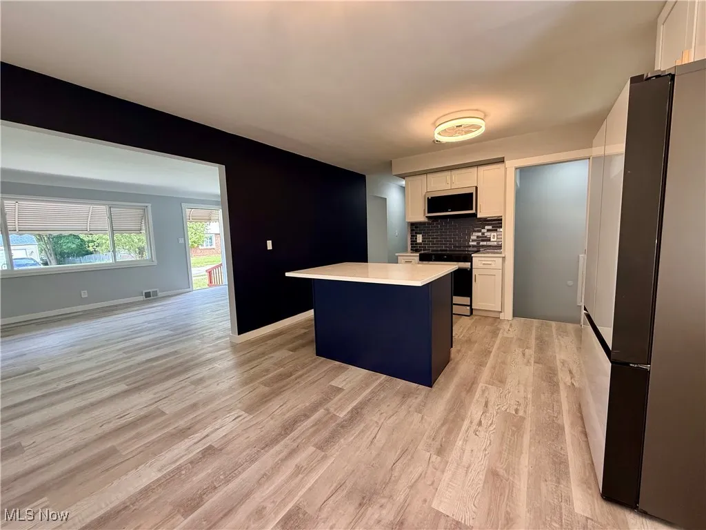 Kitchen featuring white cabinetry, tasteful backsplash, appliances with stainless steel finishes, light countertops, and light wood finished floors