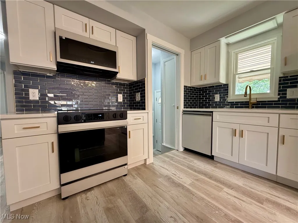 Kitchen with white cabinets, electric range oven, white microwave, and tasteful backsplash
