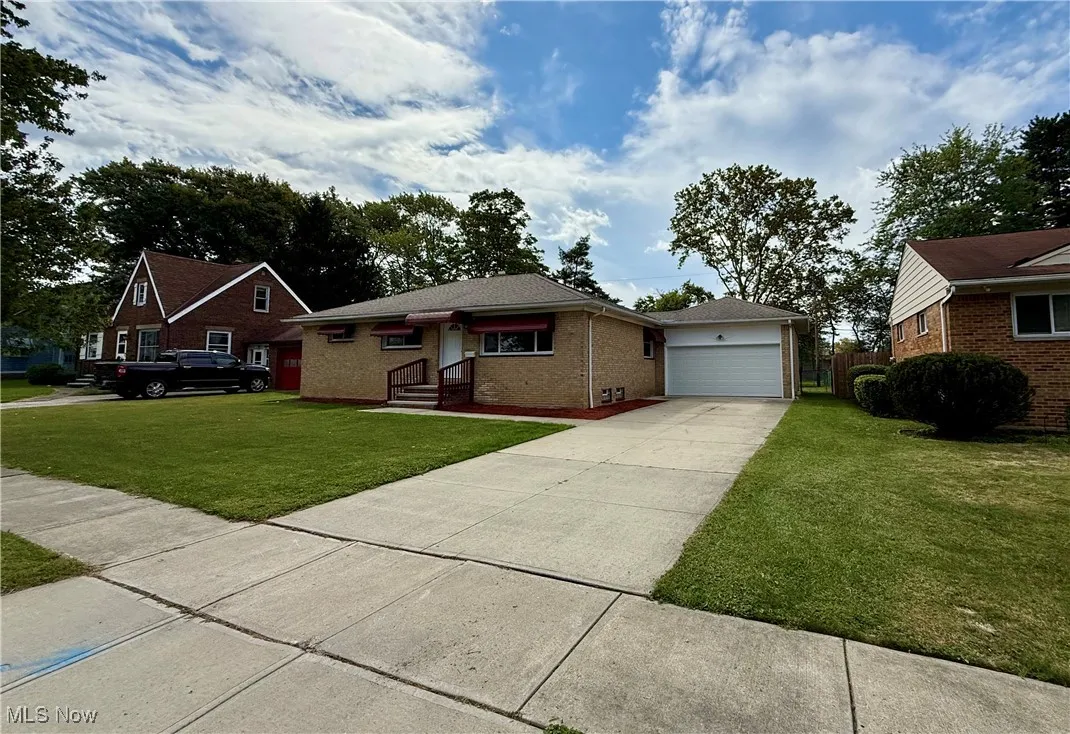 Single story home featuring brick siding, a garage, driveway, and a front yard