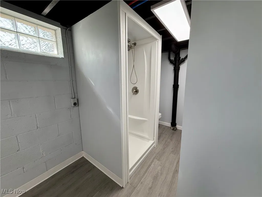 Full bath featuring a stall shower, concrete block wall, and wood finished floors