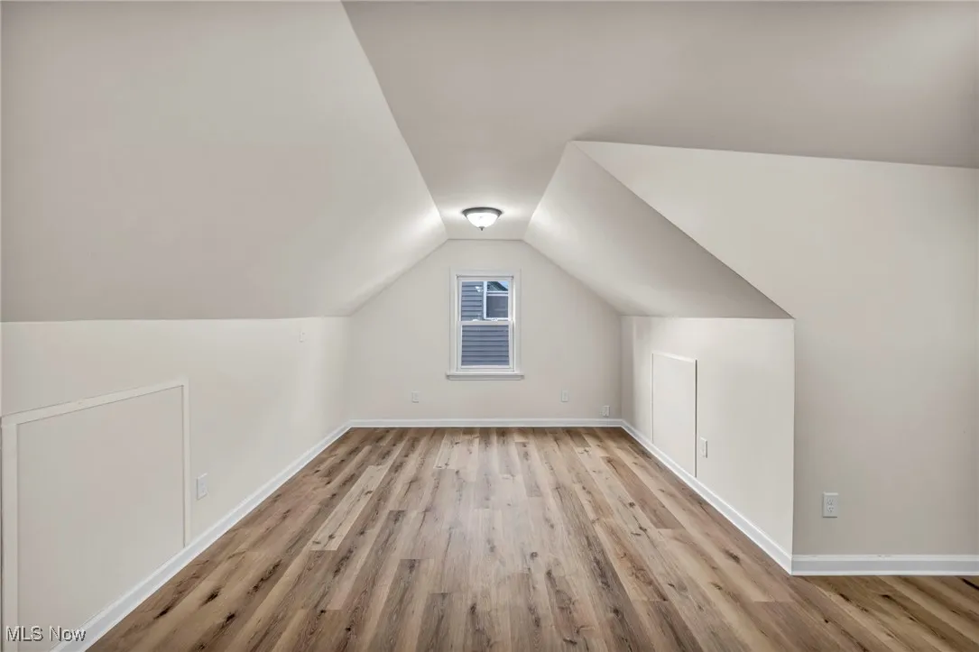 Attic bedroom featuring light wood finished floors, plenty of natural light, and vaulted ceiling