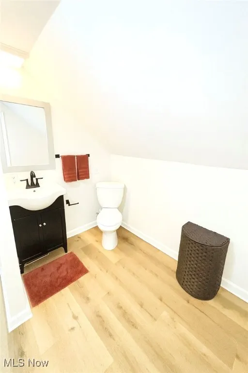 Half bath with vaulted ceiling, vanity, and light wood-style floors