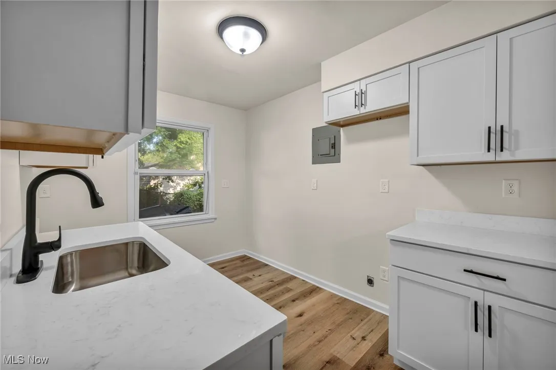 Kitchen with light wood finished floors, electric panel, light stone counters, and white cabinets