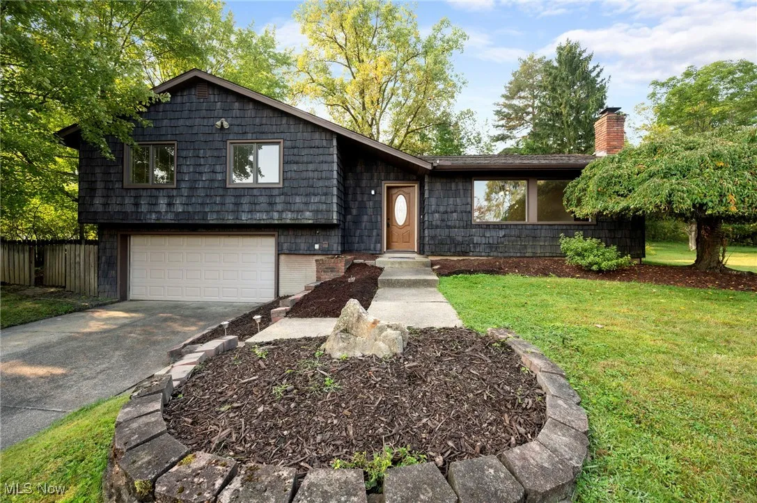 Split level home with concrete driveway, a chimney, a garage, and brick siding