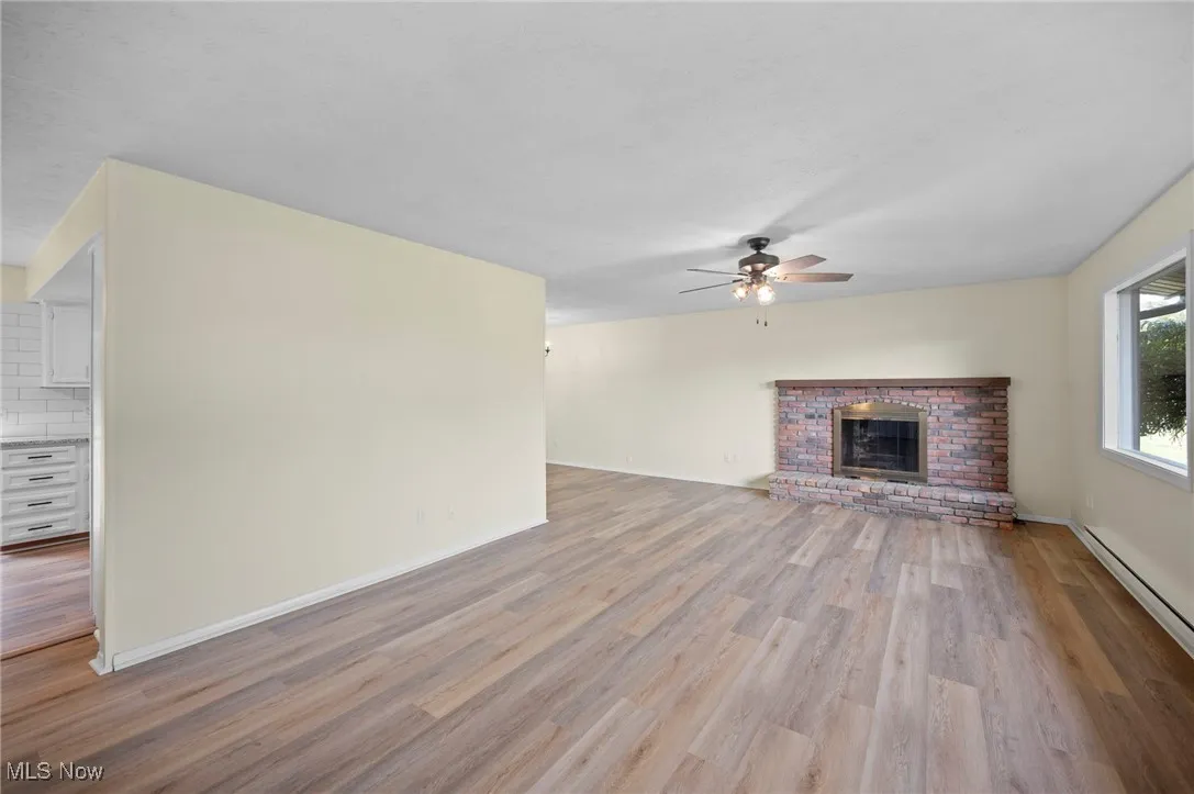 Unfurnished living room with a brick fireplace, light wood finished floors, and a ceiling fan