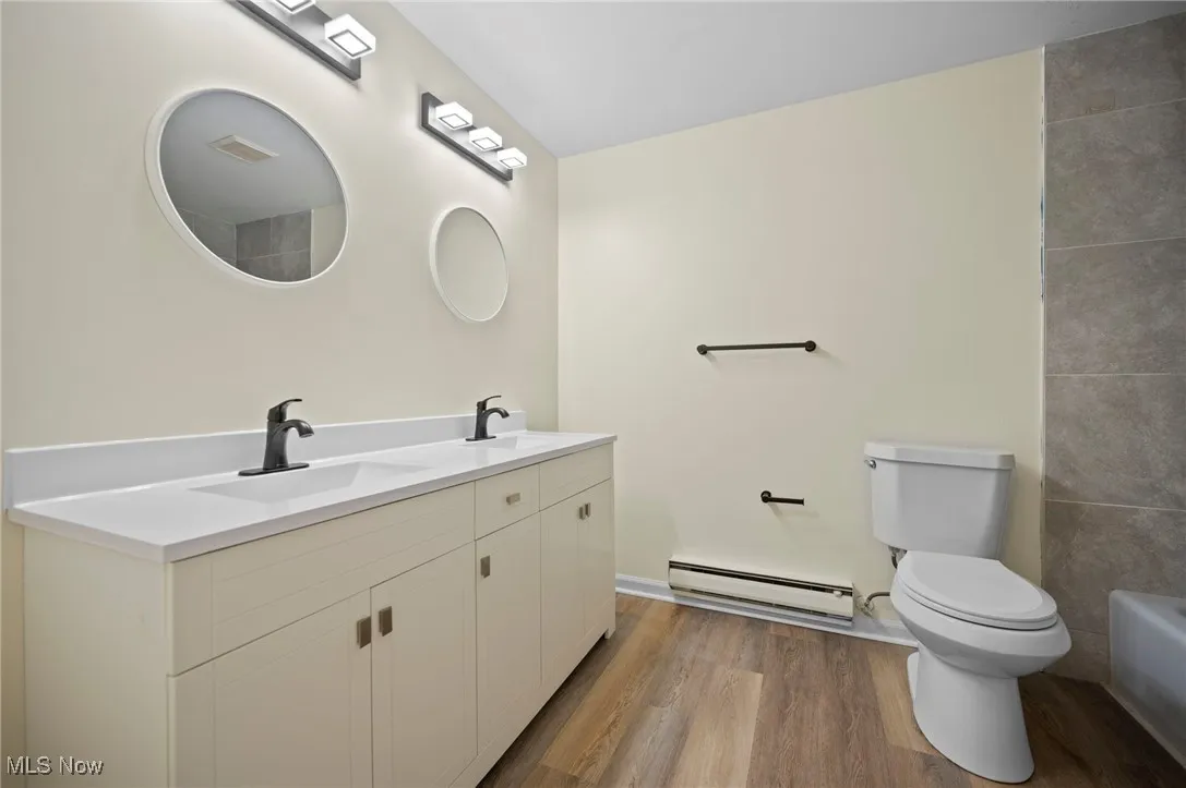 Bathroom with light wood-type flooring, a baseboard heating unit, and double vanity