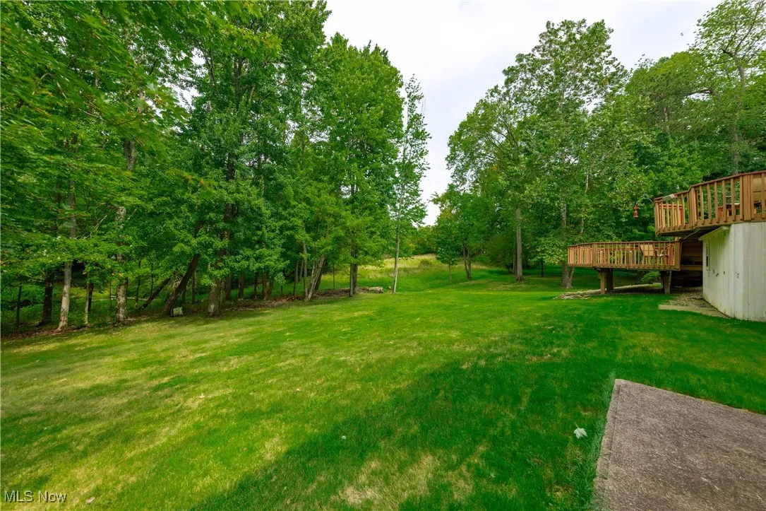 View of grassy yard with view of wooded area and a wooden deck