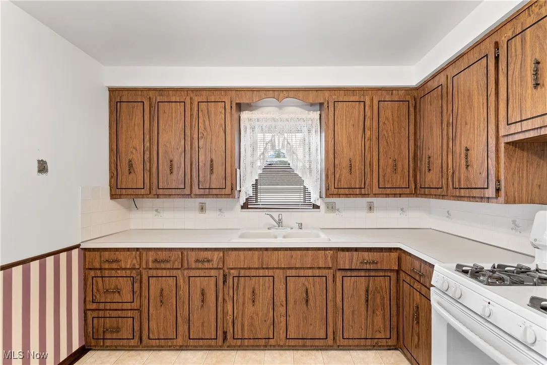 Kitchen featuring gas range gas stove, brown cabinetry, light countertops, a wainscoted wall, and decorative backsplash