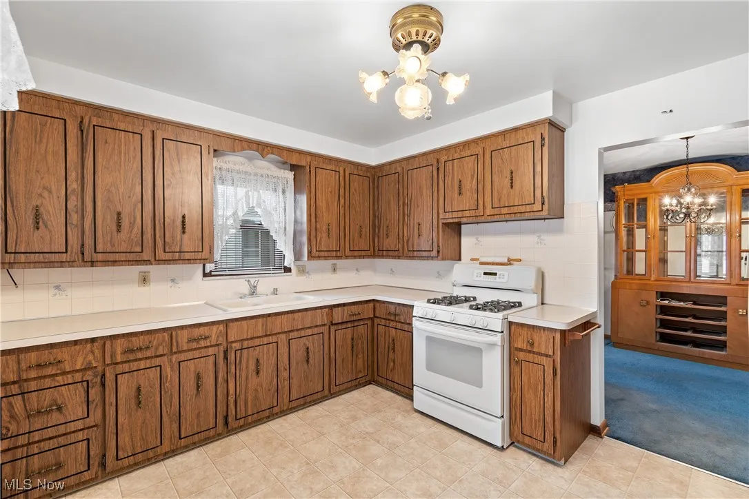 Kitchen with a chandelier, white range with gas stovetop, light countertops, and decorative light fixtures