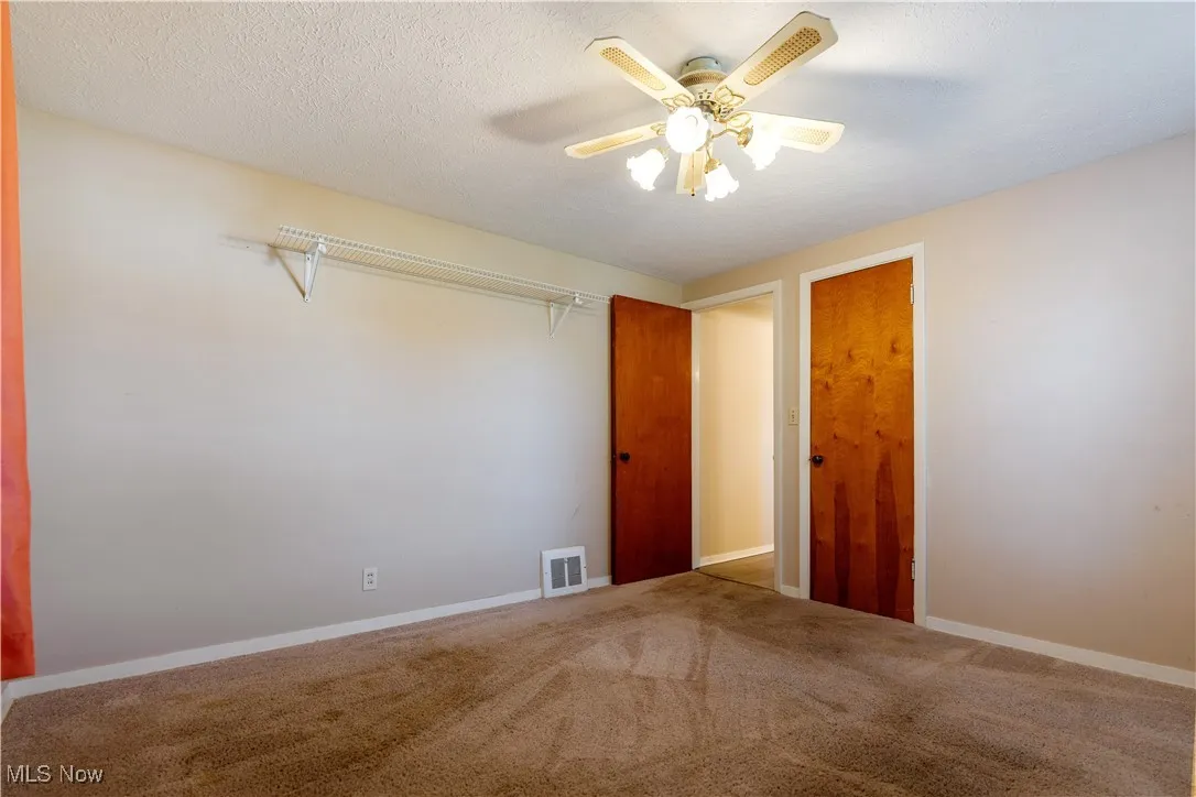 Carpeted empty room featuring a textured ceiling and a ceiling fan