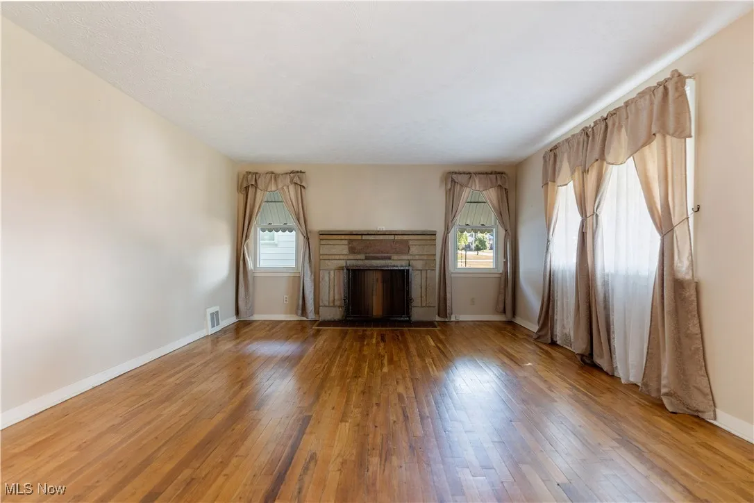 Unfurnished living room with a stone fireplace and hardwood / wood-style flooring