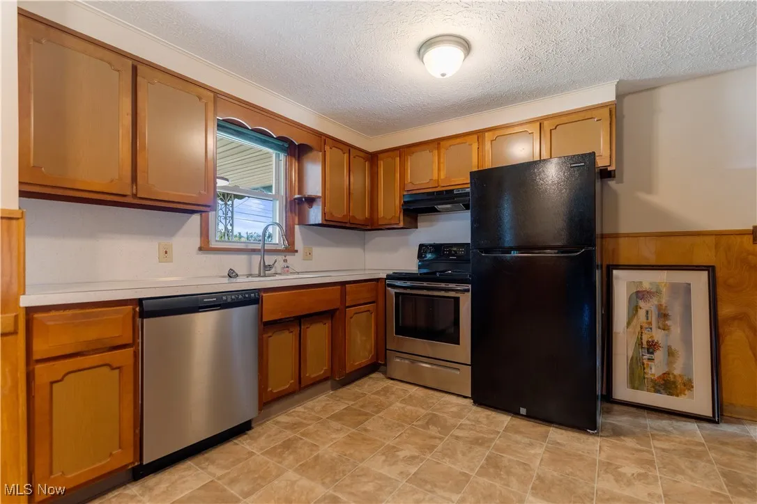 Kitchen with stainless steel appliances, light countertops, brown cabinets, a textured ceiling, and a wainscoted wall