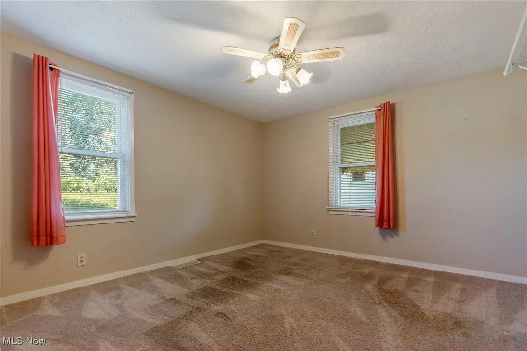 Empty room featuring carpet flooring, a textured ceiling, and ceiling fan