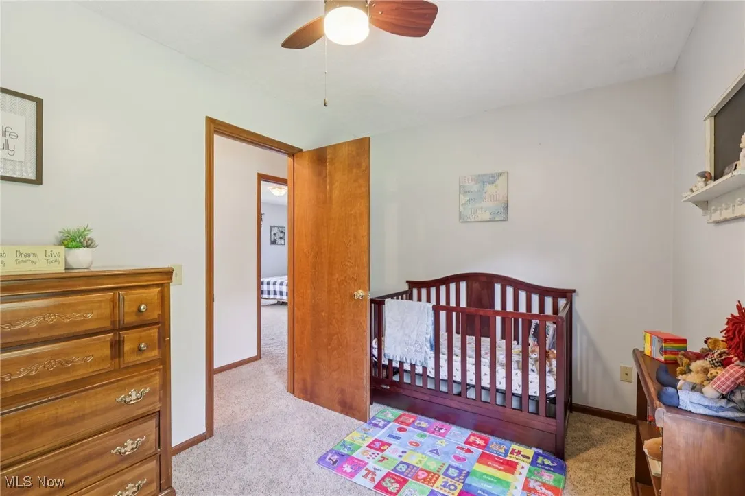 Bedroom featuring a crib, light colored carpet, and ceiling fan