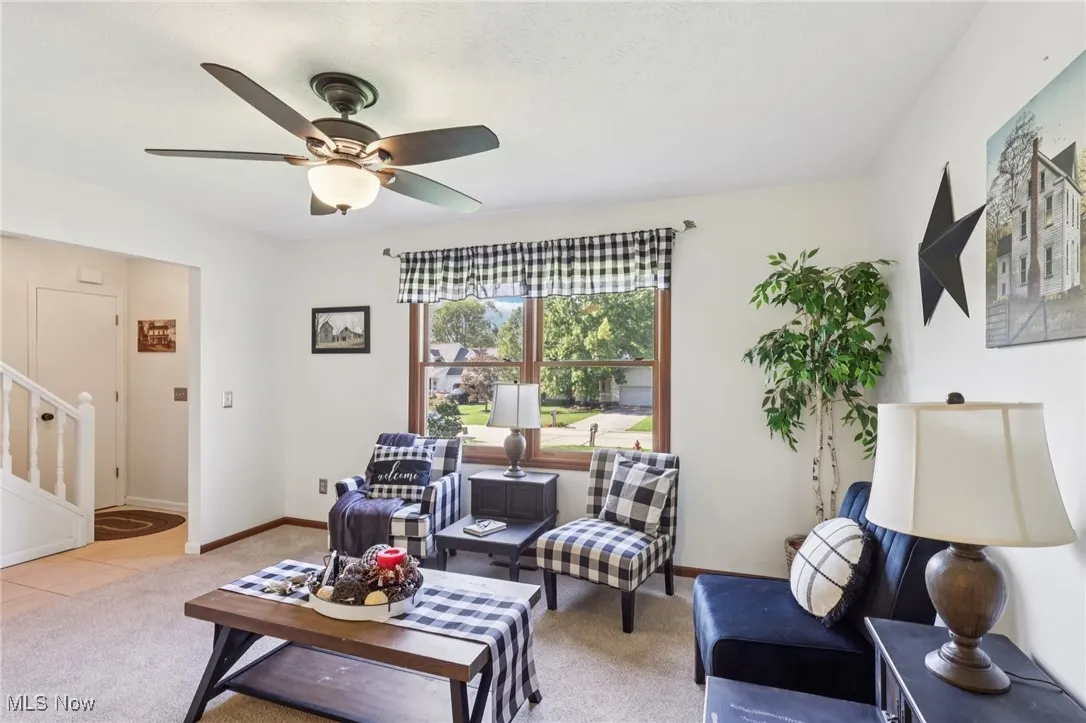Carpeted living room featuring stairway, ceiling fan, and tile patterned floors