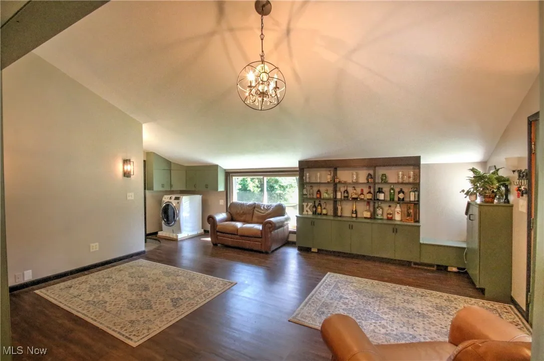 Living room with lofted ceiling, dark wood finished floors, a chandelier, and washer / clothes dryer