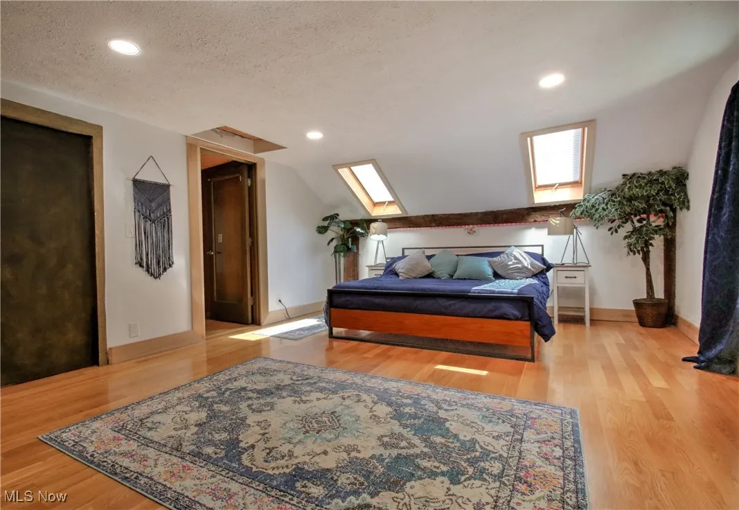 Bedroom featuring light wood-style flooring, a skylight, recessed lighting, a textured ceiling, and lofted ceiling