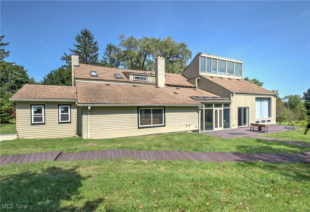 Rear view of house featuring a shingled roof, a chimney, a wooden deck, and a lawn
