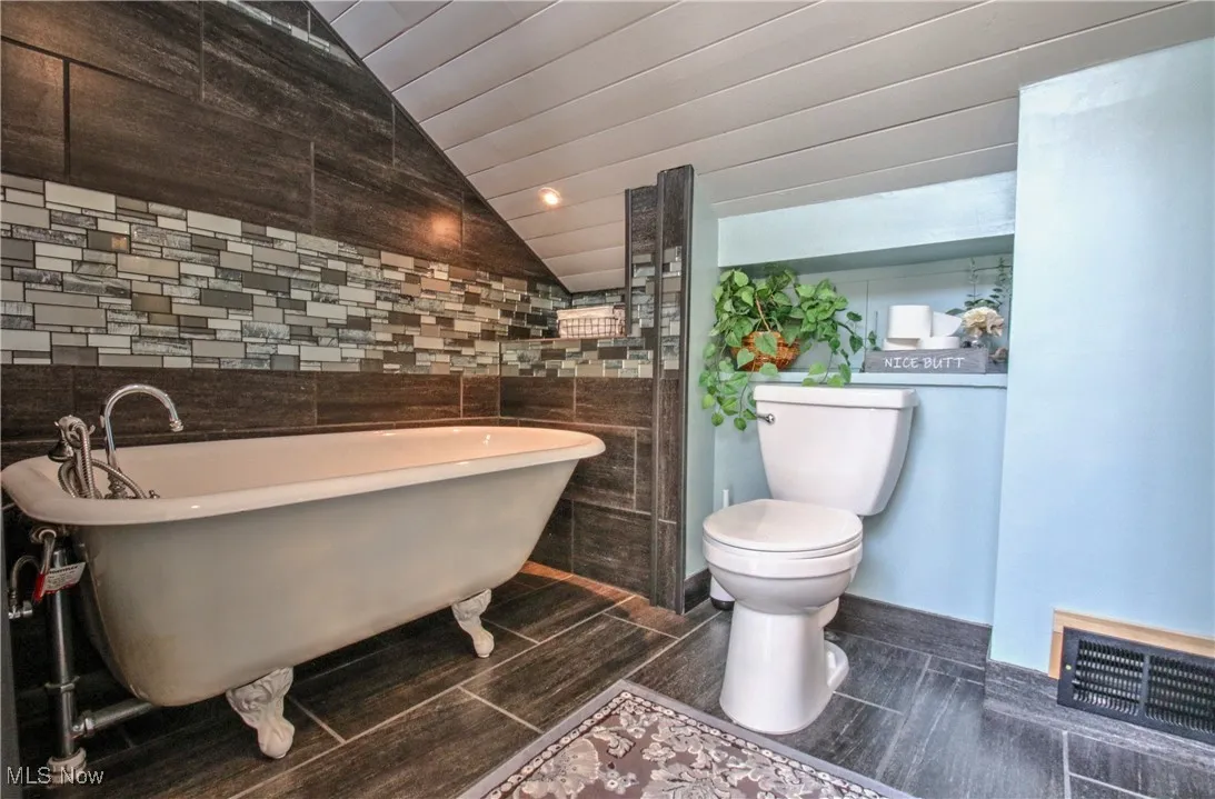 Full bath with a soaking tub, vaulted ceiling, tile walls, and recessed lighting