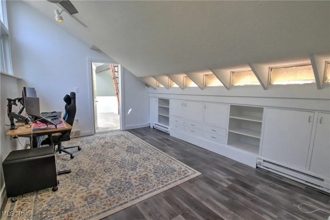 Office area with dark wood-style flooring, a baseboard radiator, vaulted ceiling, a textured ceiling, and built in shelves