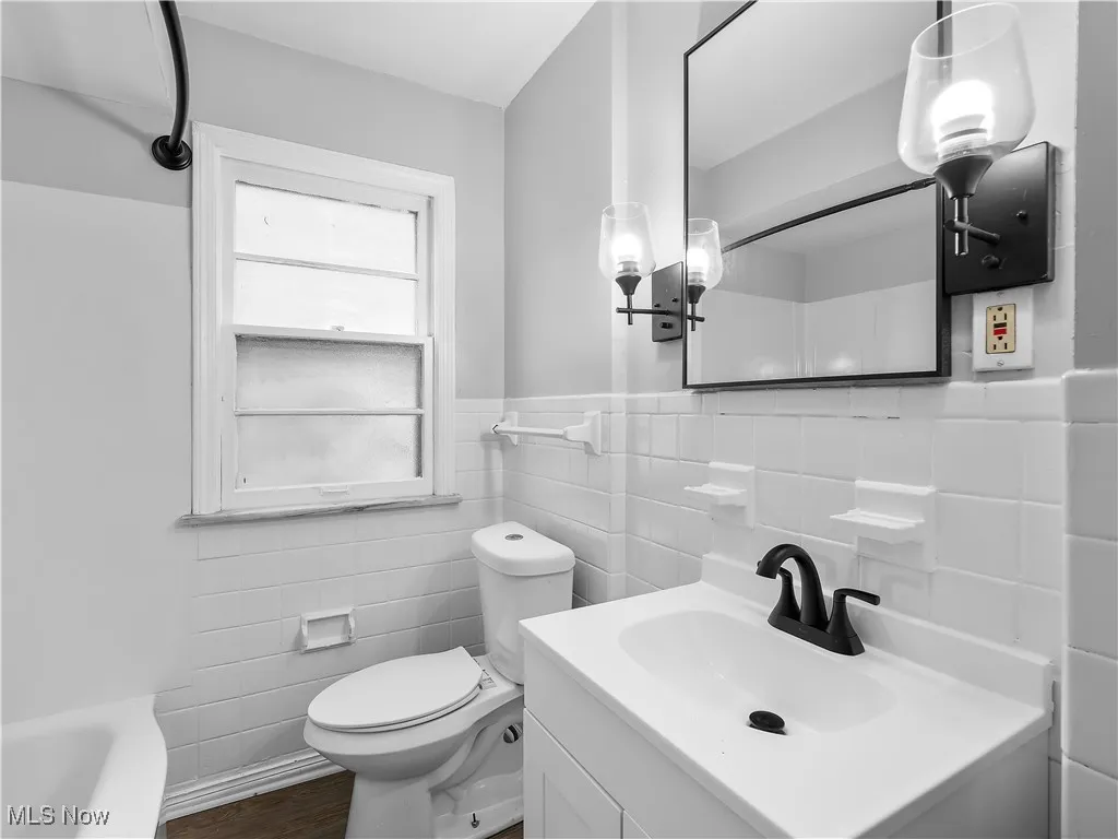 Bathroom featuring vanity, tile walls, a wainscoted wall, a bath, and dark wood-style floors