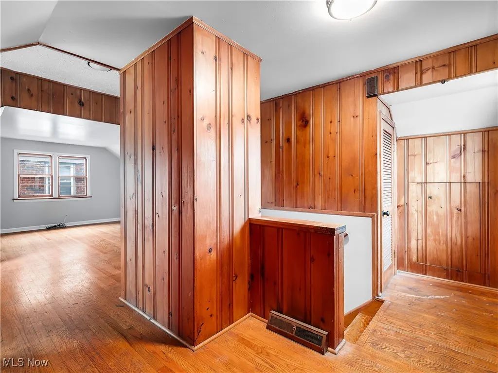 Hallway with hardwood / wood-style floors, lofted ceiling, and wood walls