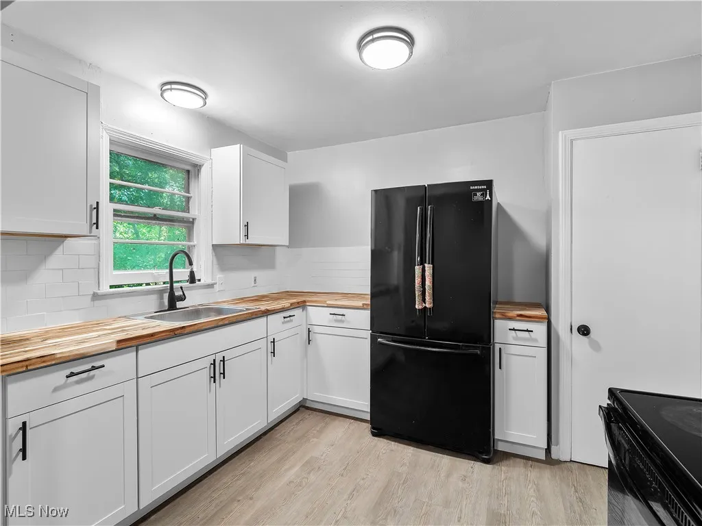 Kitchen with butcher block countertops, black appliances, white cabinetry, and light wood-style flooring