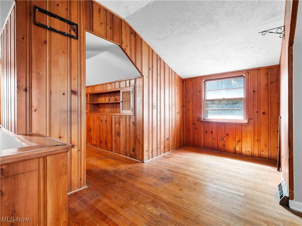 Additional living space with wood walls, light wood-style floors, vaulted ceiling, and a textured ceiling