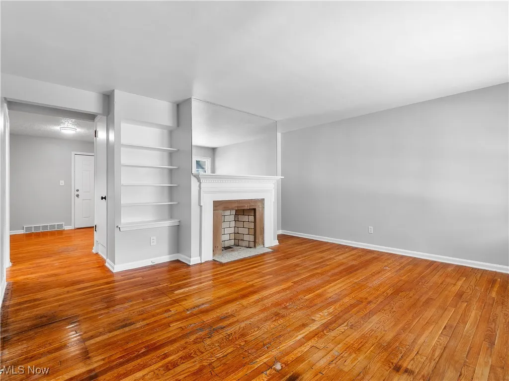 Unfurnished living room with light wood finished floors, built in features, and a fireplace with flush hearth