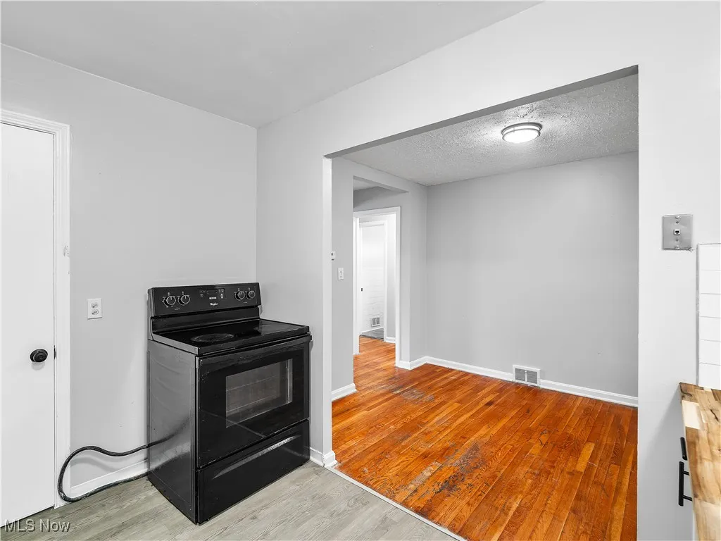 Kitchen with black range with electric stovetop, light wood-style flooring, and a textured ceiling