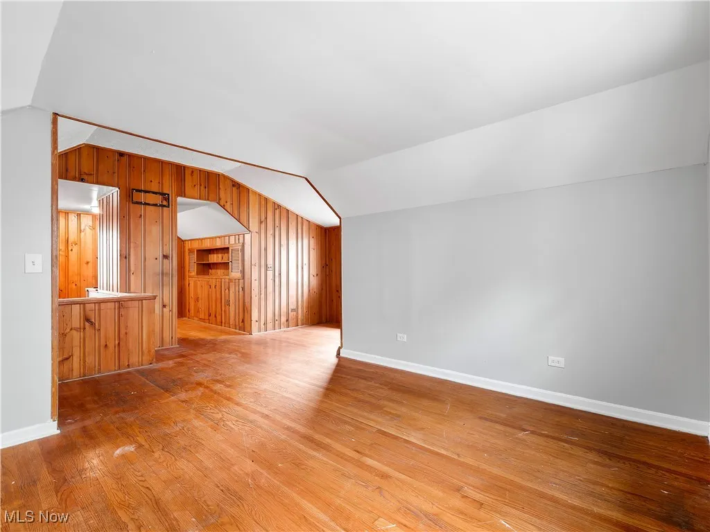 Bonus room with wood walls, vaulted ceiling, and light wood finished floors