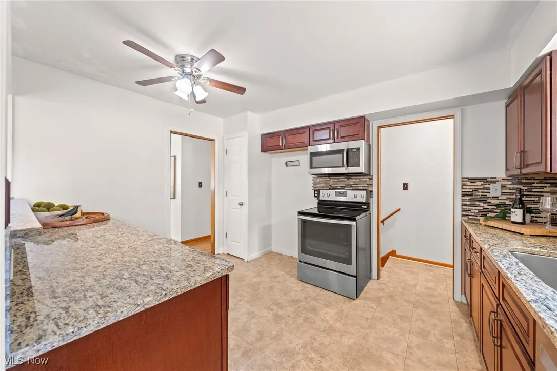 Kitchen with light stone counters, appliances with stainless steel finishes, backsplash, and a ceiling fan