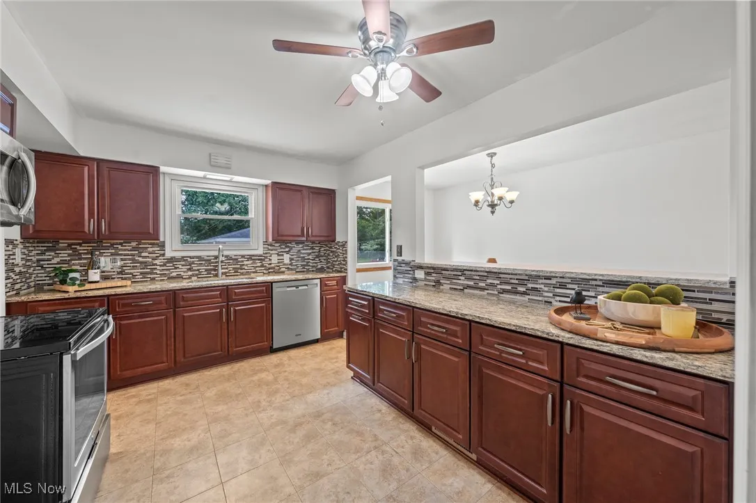 Kitchen with backsplash, appliances with stainless steel finishes, light stone counters, and dark brown cabinets