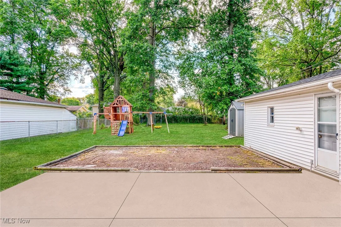 Fenced backyard featuring a playground, a storage unit, a patio area, and view of scattered trees