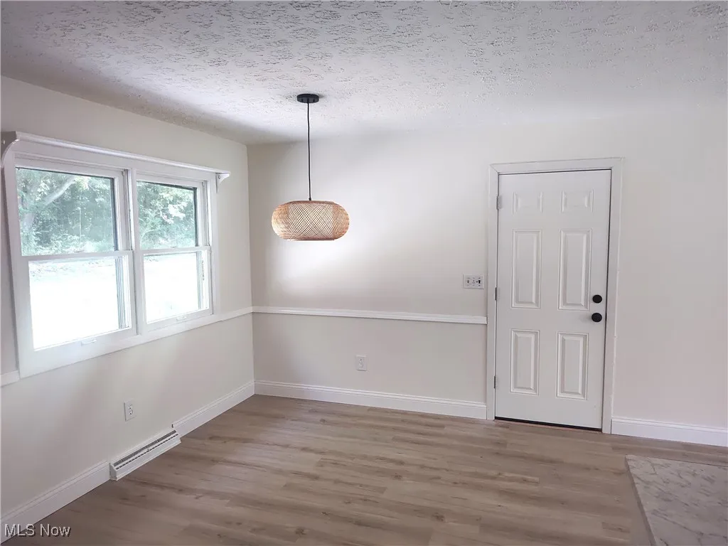 Unfurnished dining area featuring a textured ceiling, wood finished floors, and baseboard heating