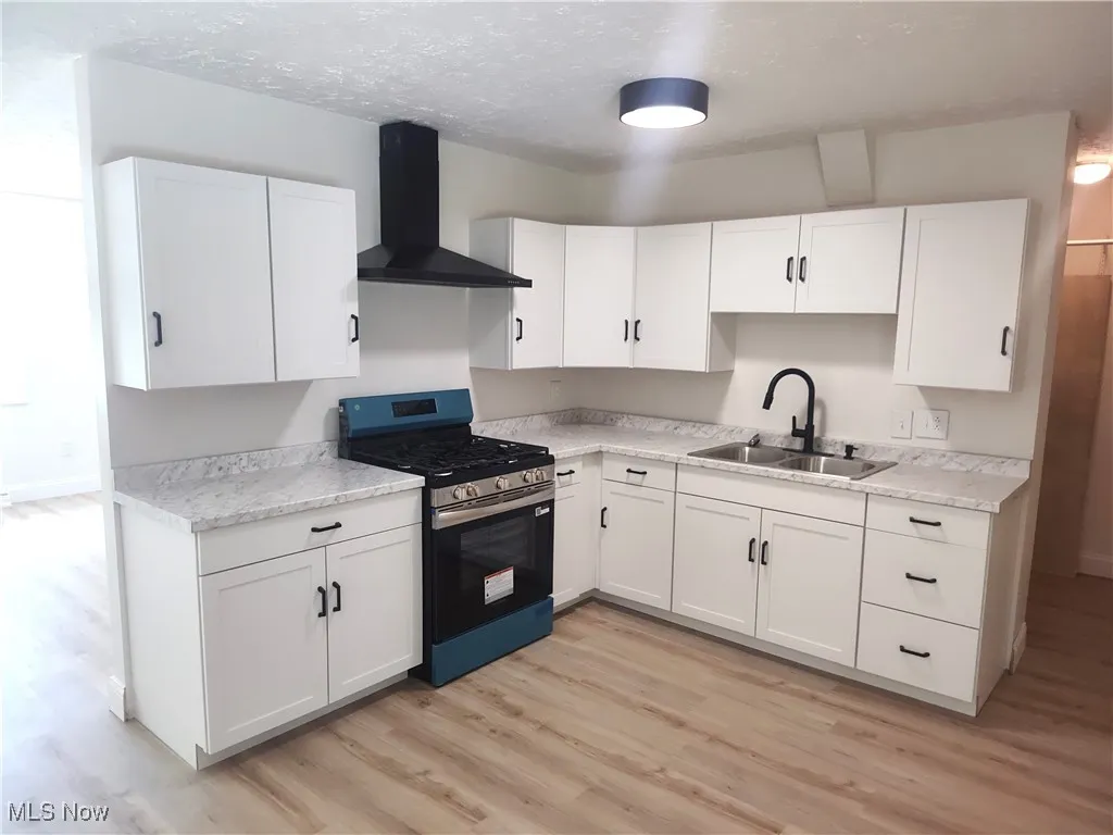 Kitchen featuring stainless steel range with gas cooktop, white cabinetry, wall chimney range hood, and a textured ceiling